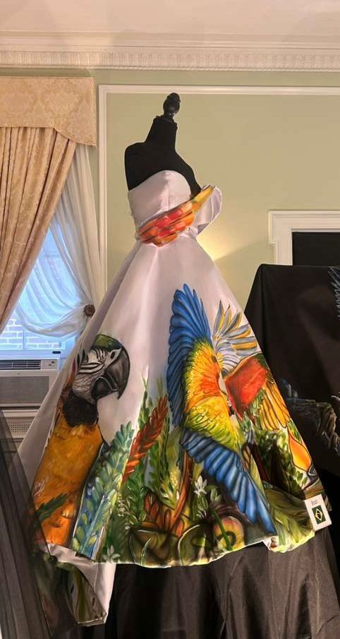 A moda brasileira ganha projeção internacional através do talento de uma estilista goiana. Um vestido assinado pela designer Maísa Gouveia foi escolhido para integrar uma exposição no museu instalado na antiga residência do ex-presidente Woodrow Wilson, reforçando o poder da moda como expressão artística e identidade nacional. A inauguração da exposição aconteceu no dia 27 de abril e segue aberta ao público reunindo criações que dialogam com cultura, história e diplomacia. O vestido de Maísa Gouveia se destaca pelo design arquitetônico e pela riqueza de detalhes. A peça ganha ainda mais força com a saia pintada à mão pelo artista plástico Selvo Afonso, que traduz em cores e formas a exuberância da fauna e da flora da Amazônia brasileira, transformando a peça em uma verdadeira obra de arte. A escolha foi feita pela diretora do museu, Elizabeth A. Karcher, que reconheceu na criação não apenas sua sofisticação estética, mas também sua potência simbólica ao unir moda, natureza e narrativa cultural. O evento, marcado por forte presença diplomática, reuniu embaixadores de diferentes países, cada um representado por peças que refletem a identidade e a tradição de suas nações. Entre os ilustres convidados, destacou-se a presença da princesa da Dinamarca, além de importantes nomes do governo, consolidando o encontro como um espaço de diálogo entre moda e relações internacionais. A criação apresentada em Washington também carrega o DNA da coleção “Aquarela de Estilos”, lançada em outubro durante desfile da Global Couture em Washington, em evento recente. Na coleção, Maísa Gouveia explora a fusão entre moda e arte com cores vibrantes e formas fluidas, inspiradas na estética das aquarelas. Ao ultrapassar as passarelas e ocupar um museu de relevância histórica, a estilista reafirma a moda como linguagem universal. Mais do que vestir, suas criações contam histórias, conectam culturas e projetam o Brasil no cenário internacional com sensibilidade, identidade e sofisticação.