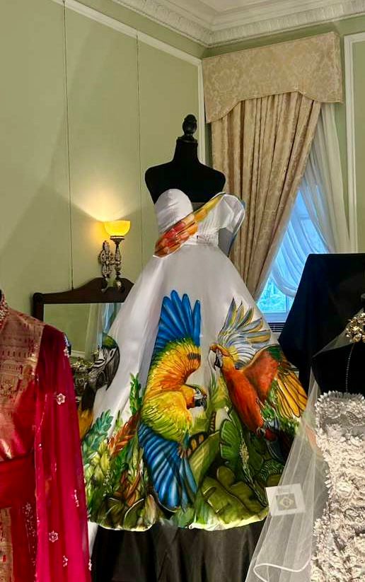 A moda brasileira ganha projeção internacional através do talento de uma estilista goiana. Um vestido assinado pela designer Maísa Gouveia foi escolhido para integrar uma exposição no museu instalado na antiga residência do ex-presidente Woodrow Wilson, reforçando o poder da moda como expressão artística e identidade nacional. A inauguração da exposição aconteceu no dia 27 de abril e segue aberta ao público reunindo criações que dialogam com cultura, história e diplomacia. O vestido de Maísa Gouveia se destaca pelo design arquitetônico e pela riqueza de detalhes. A peça ganha ainda mais força com a saia pintada à mão pelo artista plástico Selvo Afonso, que traduz em cores e formas a exuberância da fauna e da flora da Amazônia brasileira, transformando a peça em uma verdadeira obra de arte. A escolha foi feita pela diretora do museu, Elizabeth A. Karcher, que reconheceu na criação não apenas sua sofisticação estética, mas também sua potência simbólica ao unir moda, natureza e narrativa cultural. O evento, marcado por forte presença diplomática, reuniu embaixadores de diferentes países, cada um representado por peças que refletem a identidade e a tradição de suas nações. Entre os ilustres convidados, destacou-se a presença da princesa da Dinamarca, além de importantes nomes do governo, consolidando o encontro como um espaço de diálogo entre moda e relações internacionais. A criação apresentada em Washington também carrega o DNA da coleção “Aquarela de Estilos”, lançada em outubro durante desfile da Global Couture em Washington, em evento recente. Na coleção, Maísa Gouveia explora a fusão entre moda e arte com cores vibrantes e formas fluidas, inspiradas na estética das aquarelas. Ao ultrapassar as passarelas e ocupar um museu de relevância histórica, a estilista reafirma a moda como linguagem universal. Mais do que vestir, suas criações contam histórias, conectam culturas e projetam o Brasil no cenário internacional com sensibilidade, identidade e sofisticação.